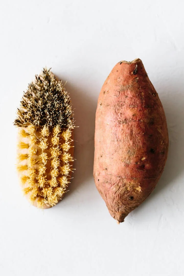 A sweet potato next to a cleaning brush.