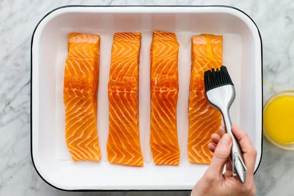 Baked salmon fillets with butter being brushed onto them.