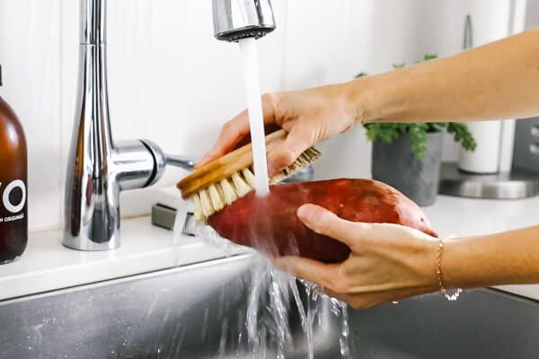 Washing the sweet potato under the faucet.