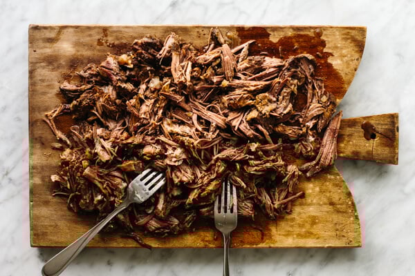 Shredding beef barbacoa on a cutting board.