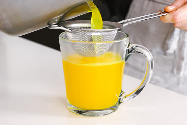 Straining the turmeric tea into a glass.