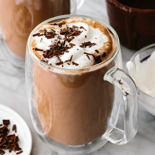 A glass of Nutella hot chocolate next to whipped cream.