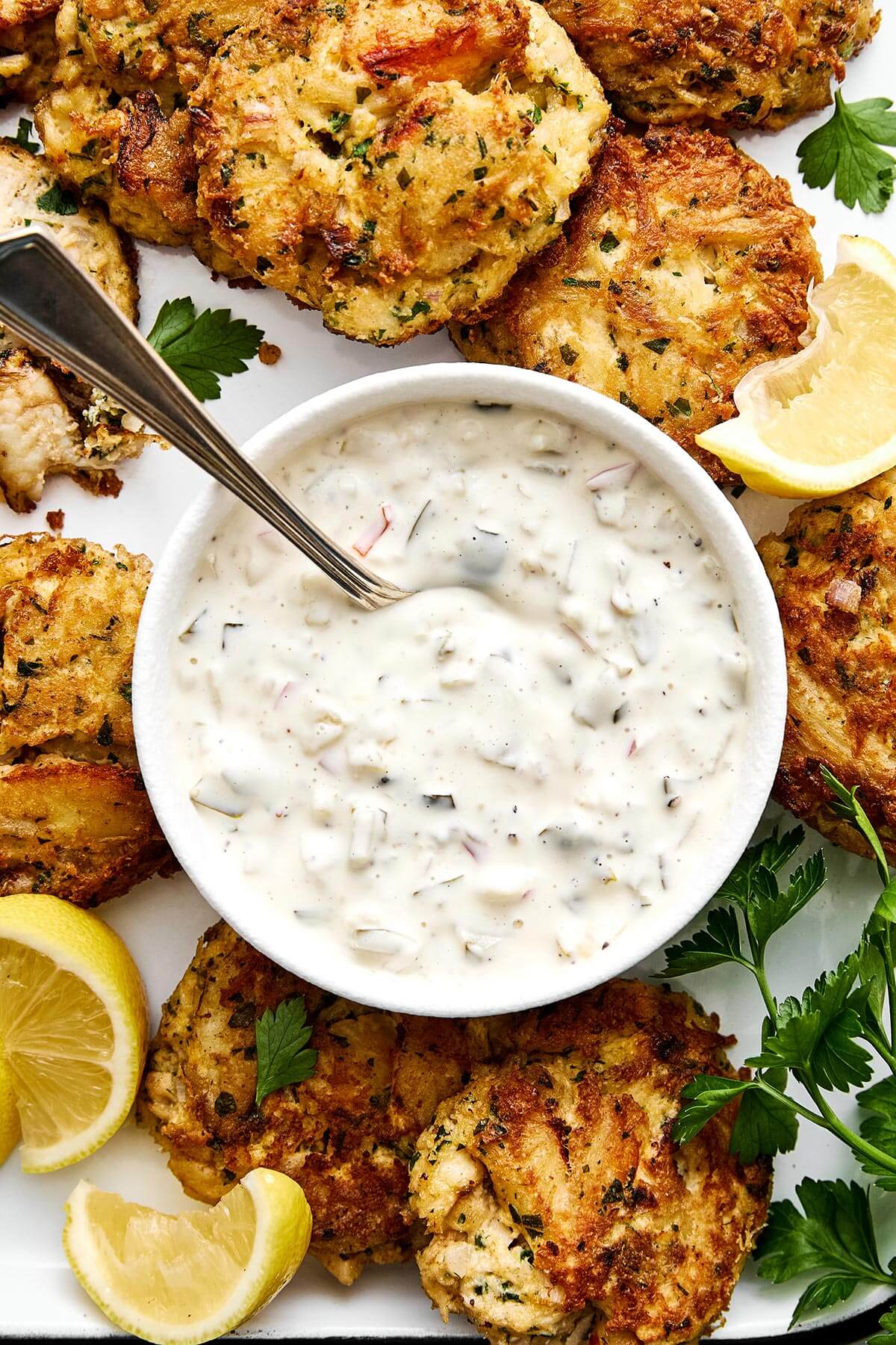 A bowl of tartar sauce with crab cakes.