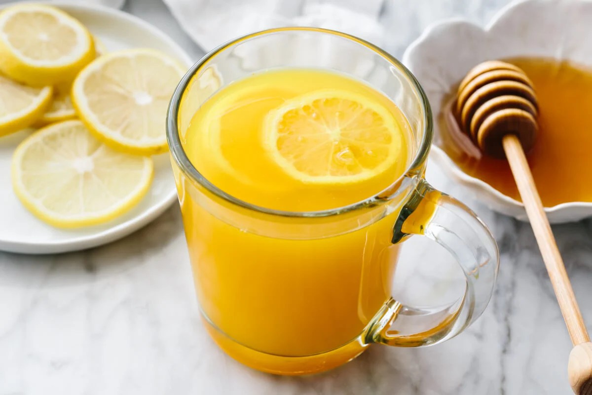 Turmeric tea in a glass with honey and lemon slices in the background.